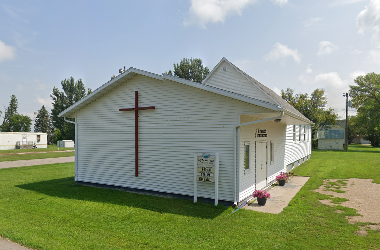 Ny Stavanger Lutheran Church in Buxton, with a cross on its white exterior and flowers beside the entrance